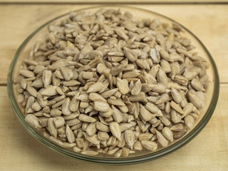 Peeled sunflower seeds in a glass plate on a wooden background
