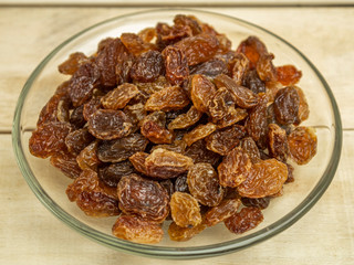 Raisins in a glass plate on a wooden background