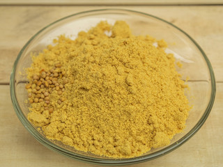 Seasoning mustard powder in a glass plate on a wooden background