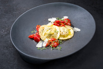 Traditionelle italienische Ravioli Pasta angeboten mit Parmesan Käse und gebratene Tomaten als closeup auf einem Modern Design Teller