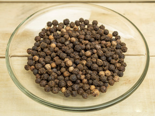 Spice pepper black peas in a glass plate on a wooden background
