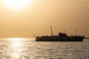 Fototapeta premium Cruise ship in the middle of the sea at sunset. He retreated in the backlight and towards the sun.