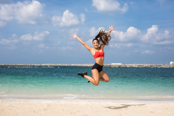 Fitness woman jumping on the beach with arms out on a sunny day