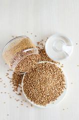 vertical. sprinkled buckwheat porridge from glass jar on white wooden background, copy space. healthy and nutritious food. crisis, hunger. vegetarianism