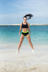 Young fitness woman jumping exercises on the beach