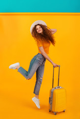 happy girl with a passport, plane tickets and a suitcase on an isolated yellow background.