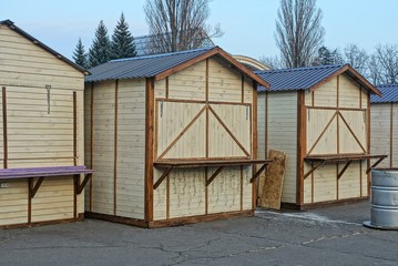 a row of brown wooden stalls stand on gray asphalt in a city street