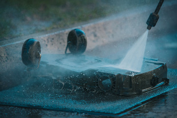 Man cleaning the underside of a robotic autonomous lawnmower with the help of a high pressure jet...