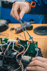Serviceman replacing water seals on robotic lawnmower, motorized lawnmower being serviced on a table after a year of use in the mud and grass. Regular maintenance of robotic lawnmower