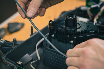 Serviceman replacing water seals on robotic lawnmower, motorized lawnmower being serviced on a table after a year of use in the mud and grass. Regular maintenance of robotic lawnmower