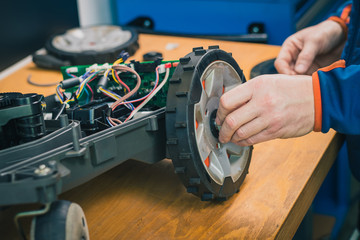 Serviceman replacing wheels  on robotic lawnmower, motorized lawnmower being serviced on a table after a year of use in the mud and grass. Regular maintenance of robotic lawnmower