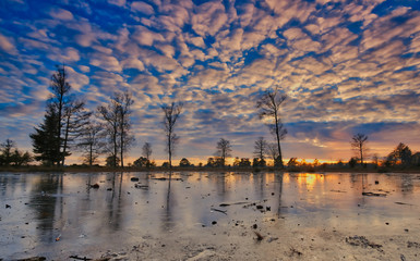 Obraz premium A cold sunset in winter on a frozen lake with a beautiful sky and sunbeams in the background Friesland, The Netherlands