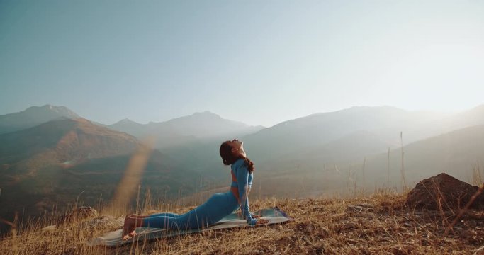 Yoga session in mountains. Young athletic girl training in cliffy mountains during sunrise, doing various yoga poses - healthy lifestyle concept 4k footage
