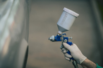 Caucasian man is spraying color with a compressed air paint gun on the vintage car as a restoration...