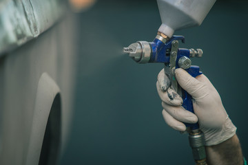 Man with automotive air spray gun in action during the restoration of a vintage car. Applying first...