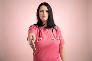 Fototapeta premium Beautiful woman doctor with stethoscope, wearing pink scrubs shaking hand