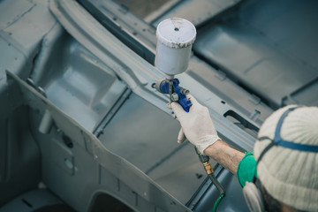 Man with automotive air spray gun in action during the restoration of a vintage car. Applying first...