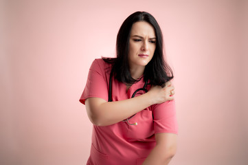 Obraz premium Beautiful woman doctor with stethoscope, wearing pink scrubs has shoulder pain