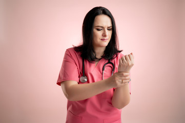 Beautiful woman doctor with stethoscope, wearing pink scrubs has wrist pain