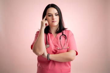 Beautiful woman doctor with stethoscope, wearing pink scrubs wondering