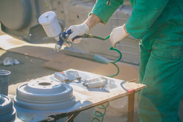 Man with automotive air spray gun in action during the restoration of a vintage car. Applying first base layer of paint onto used drum brakes.