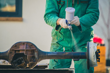 Man with automotive air spray gun in action during the restoration of a vintage car. Applying first...