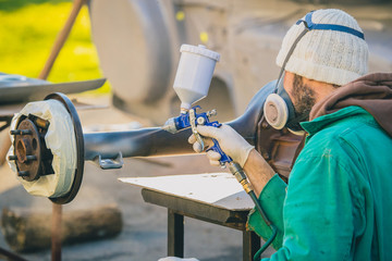 Man with automotive air spray gun in action during the restoration of a vintage car. Applying first base layer of paint onto an old big differential unit or rear axle.