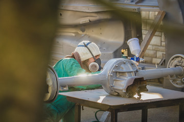 Man with automotive air spray gun in action during the restoration of a vintage car. Applying first...