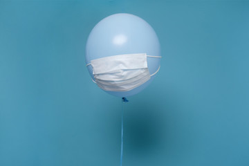 Blue balloon with medical mask on it hanging on air on blue wall.