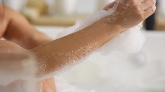 Unrecognized woman washing body with foam at bath. Woman hands touching skin
