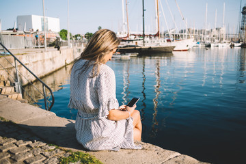 Young lady sitting with cellphone on city seafront