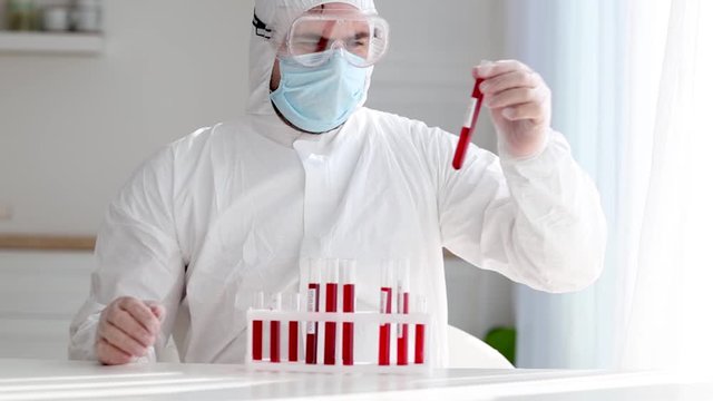 man in protective medical outfit working in laboratory with test tubes, analysing samples