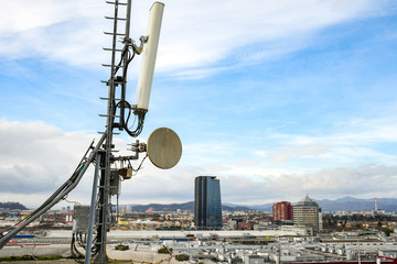 Cellular radio telecommunication network antenna mounted on a metal pole providing strong signal waves from the top of the roof across big city 