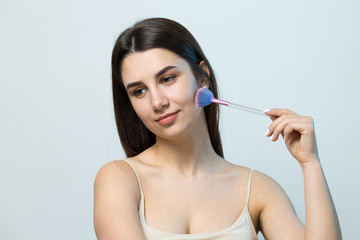 Close-up of a young girl in a light top on a white background making a facial make-up. A pretty...