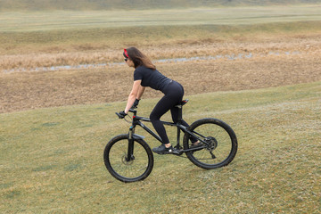 Girl on a mountain bike on offroad, beautiful portrait of a cyclist in rainy weather, Fitness girl rides a modern carbon fiber mountain bike in sportswear. Close-up portrait of a girl in red bandana.