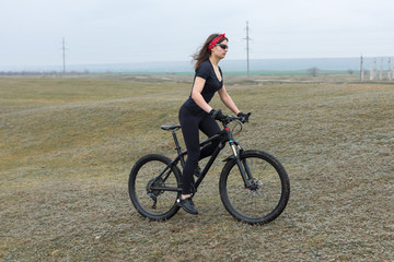 Girl on a mountain bike on offroad, beautiful portrait of a cyclist in rainy weather, Fitness girl rides a modern carbon fiber mountain bike in sportswear. Close-up portrait of a girl in red bandana.