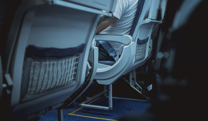 Lower portion of an aeroplane seat with mesh pockets visible and person sitting in a chair.