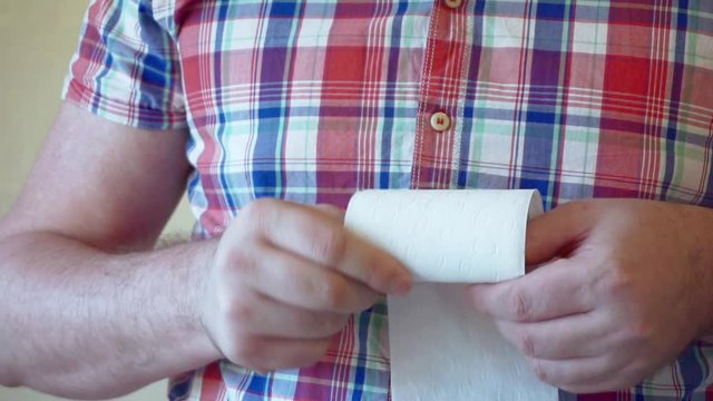 Men's hands unwind a roll of white toilet paper.