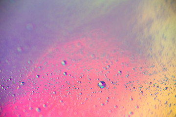 A lot of small drops of water on a colorful pastel holographic background.