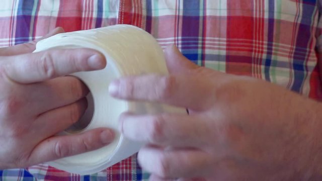 Men's hands unwind a roll of white toilet paper.