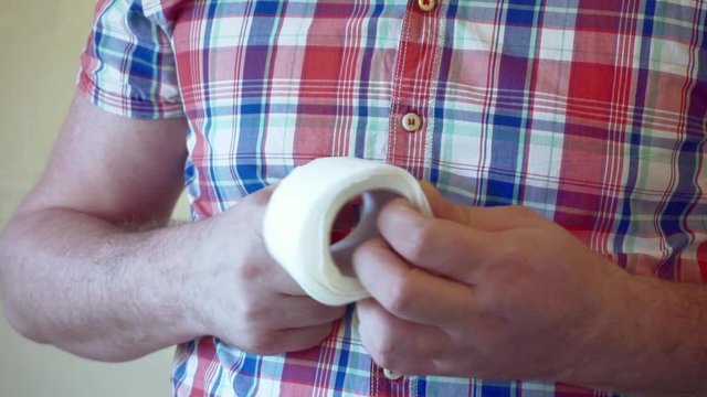 Men's hands unwind a roll of white toilet paper.