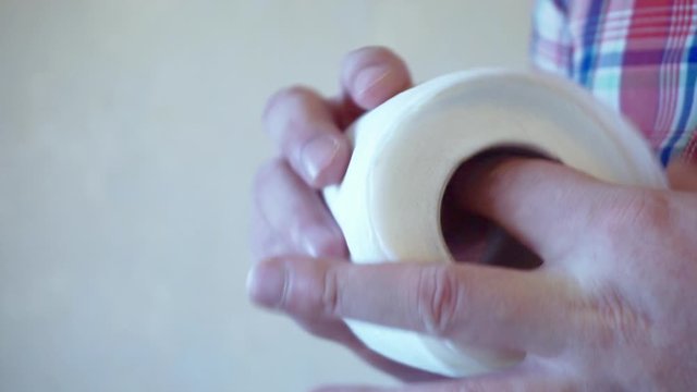 male hands hold a roll of white toilet paper.