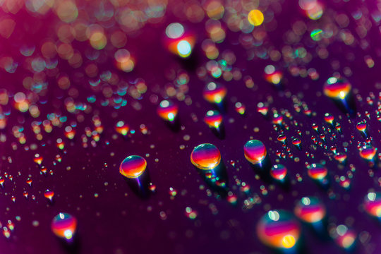 Closeup rainbow drops of water on a vibrant purple background with sparkling bokeh.