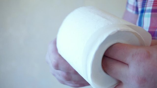Men's hands unwind a roll of white toilet paper