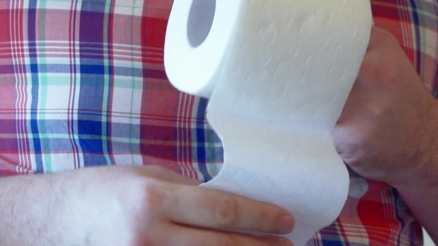 Men's hands unwind a roll of white toilet paper