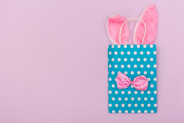 Minimalistic pastel image with blue gift bag with Easter bunny ears and the bow tie on pink background with copy space.