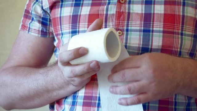 male hands hold a roll of white toilet paper.