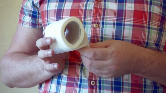 male hands hold a roll of white toilet paper.