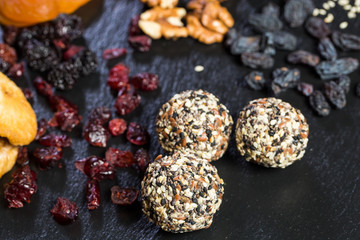 Theme sweet dessert made from natural products without sugar. Macro close-up of deserts ball round candy truffle on a black plate with natural dried fruit and seeds of white and black sesame and flax