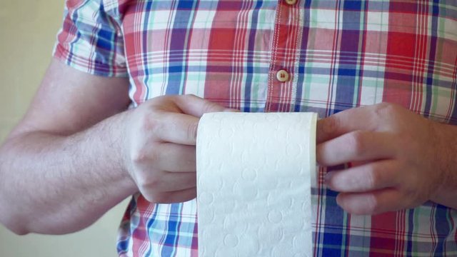 male hands hold a roll of white toilet paper.